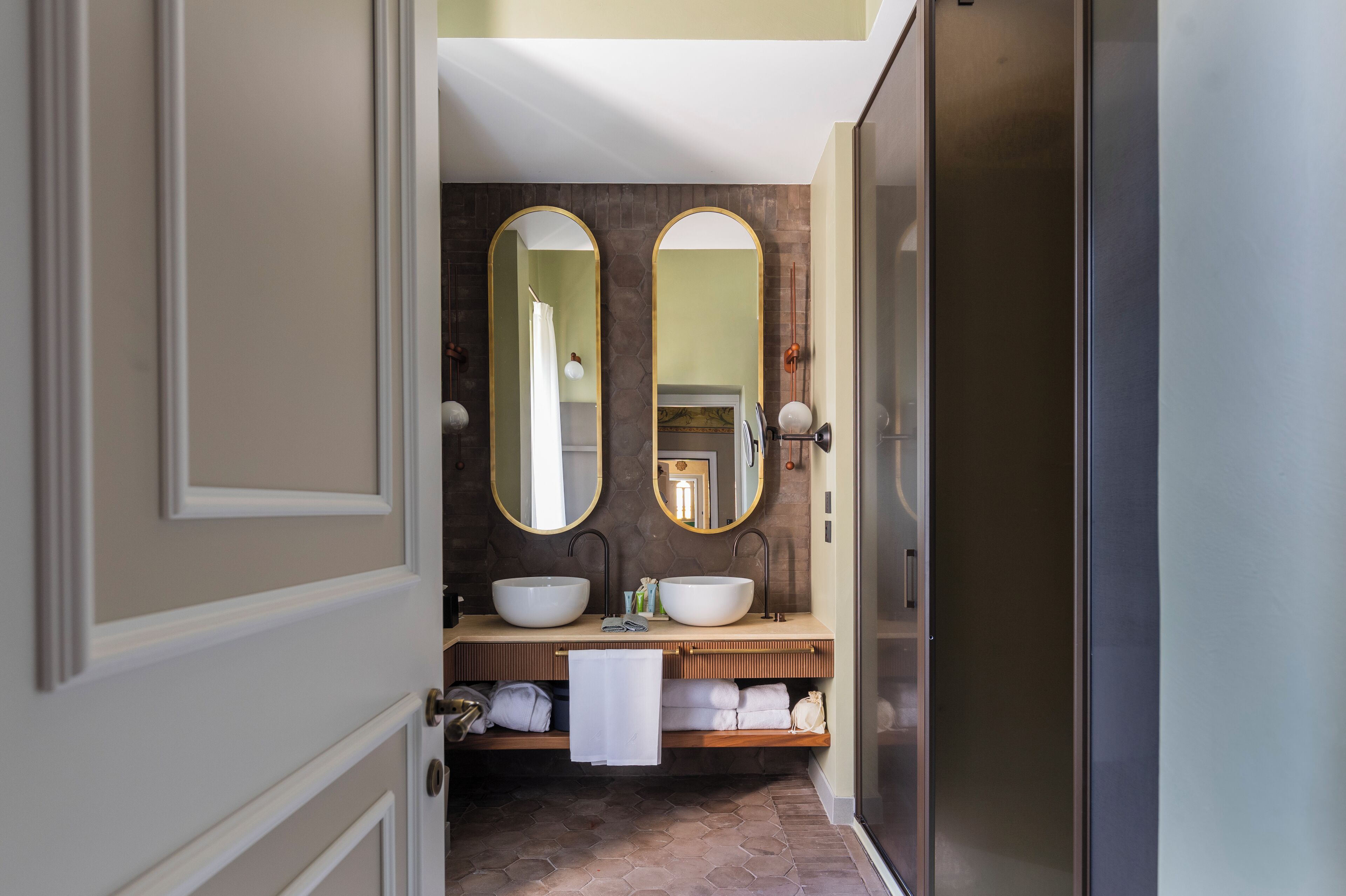 Un baño moderno con dos espejos ovalados grandes, un mueble de tocador doble y un perchero para toallas.