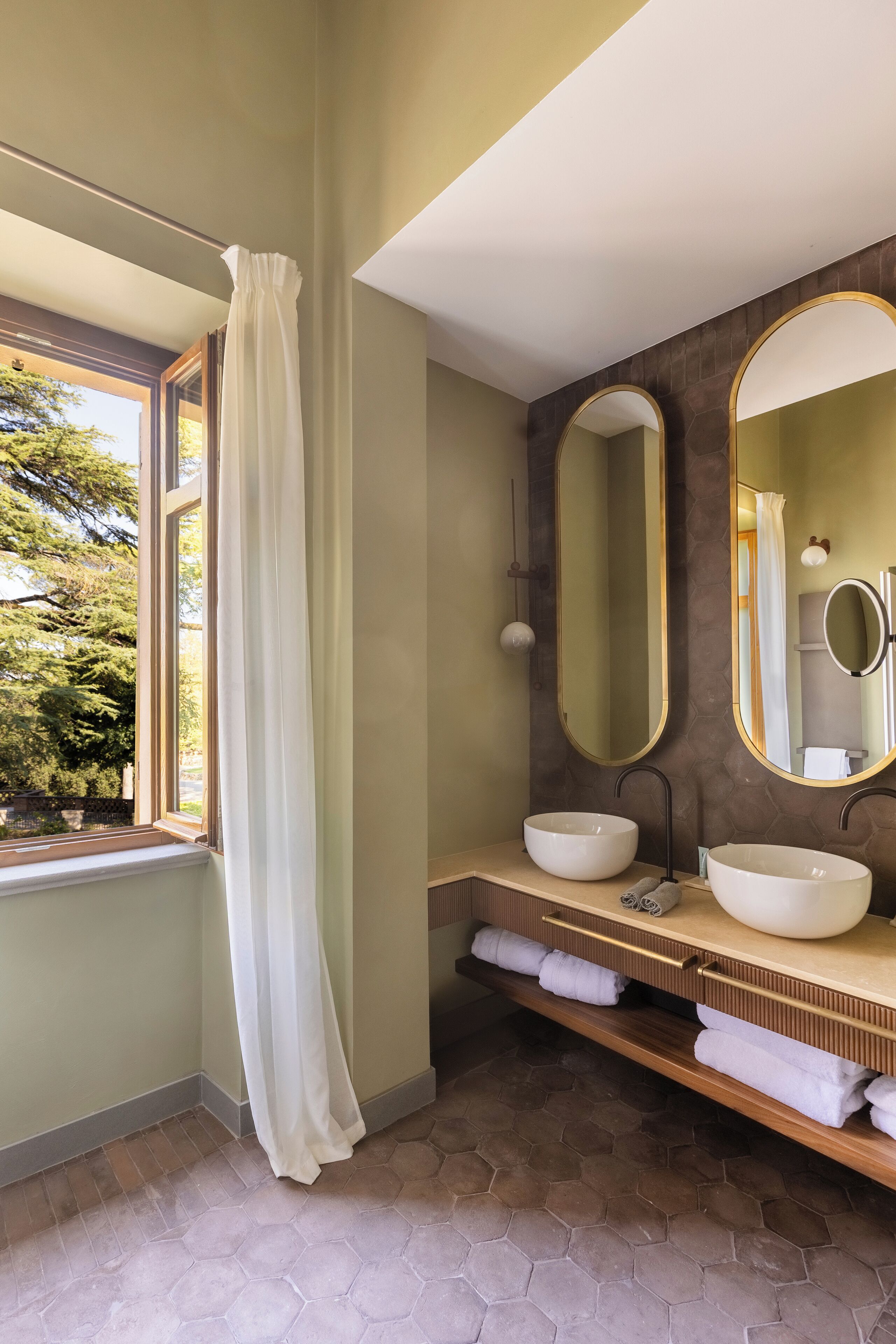 A bathroom with two sinks, a large mirror, and a window with a white curtain.