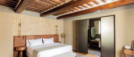 Un dormitorio con una cama grande, vigas de madera en el techo, un baño con bañera y un espejo.