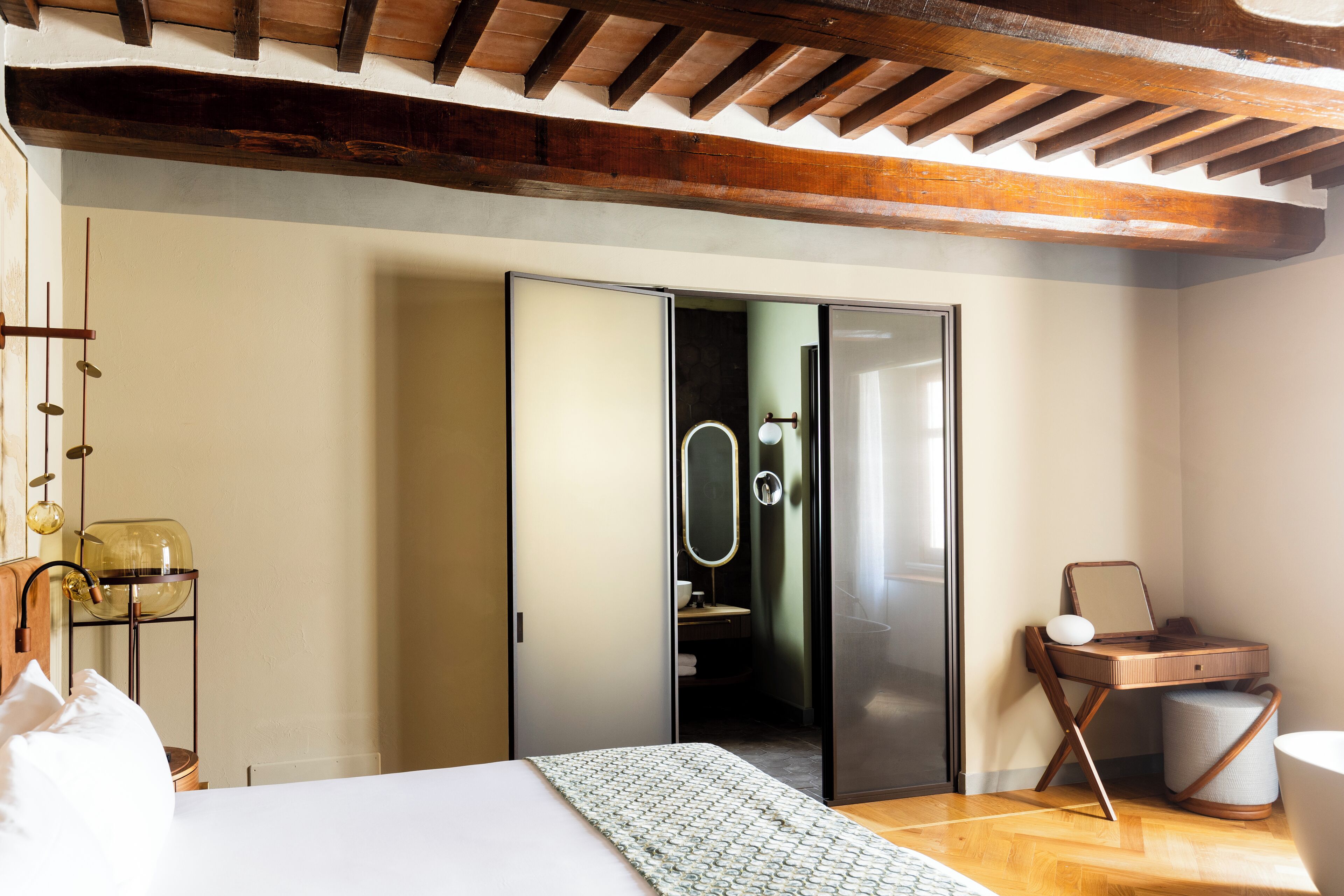 A modern bedroom with a bed, a bedside table, a lamp, a mirror, and a wooden ceiling.