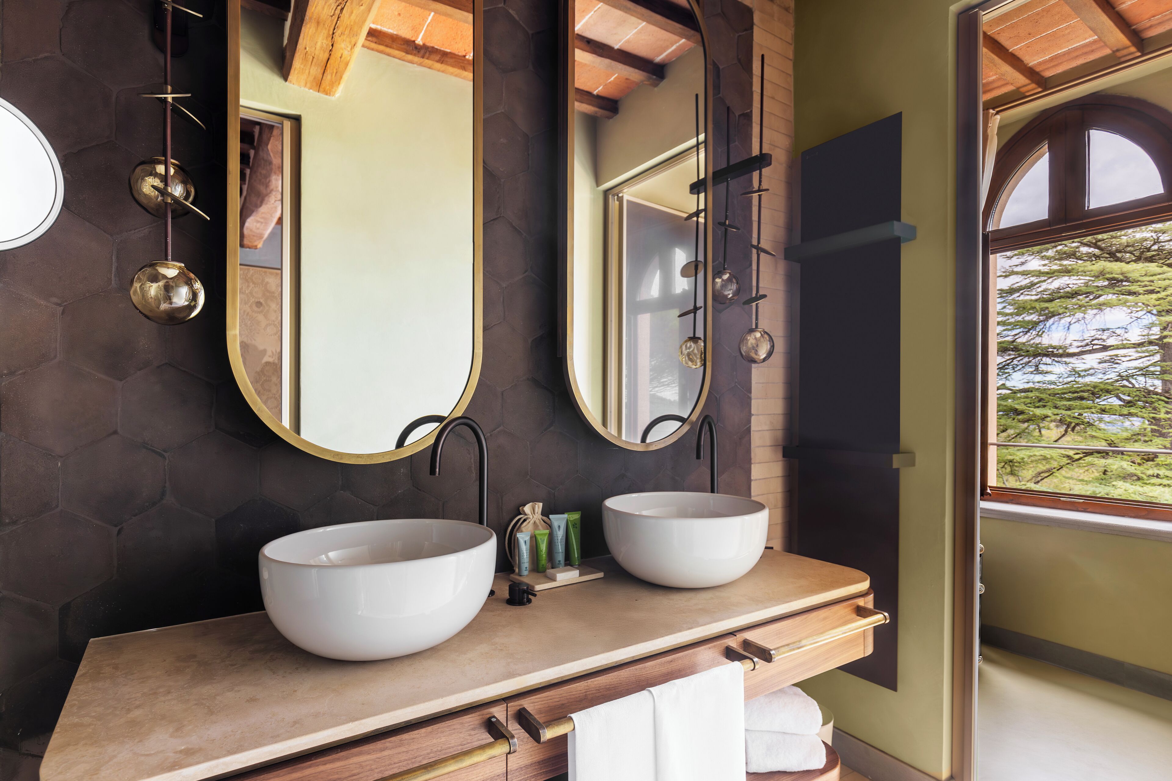 A bathroom with two large white sinks, a mirror, and a window with a view of trees.