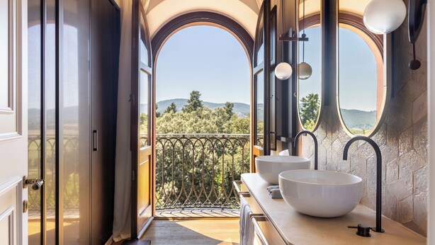 A bathroom with two large white sinks, a mirror, and a view of a balcony with a railing. - Borgo Dei Conti Resort Relais & Chateaux (Perugia)