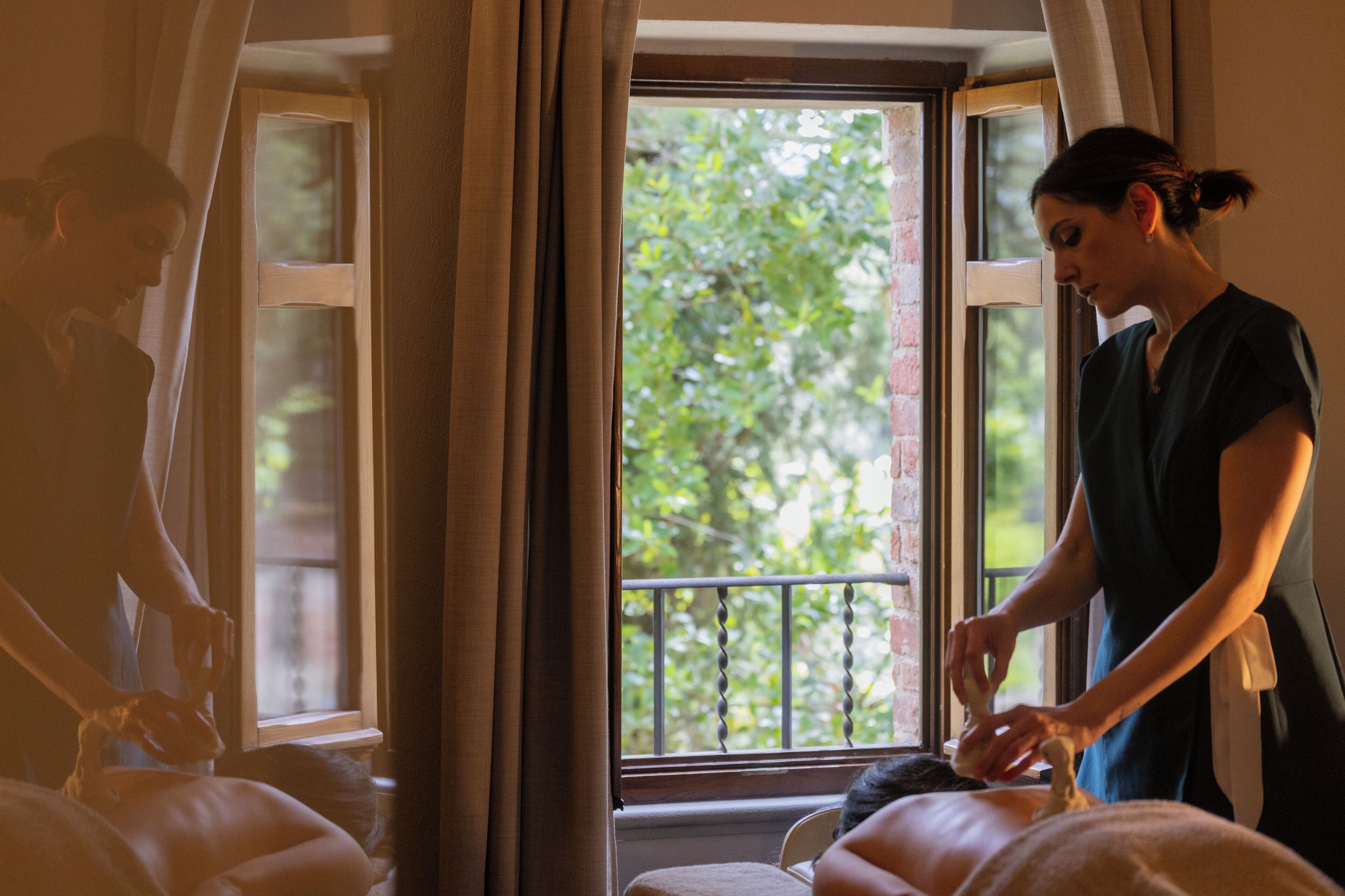 Una habitación con camilla de masaje, una ventana con cortinas y vistas al exterior.