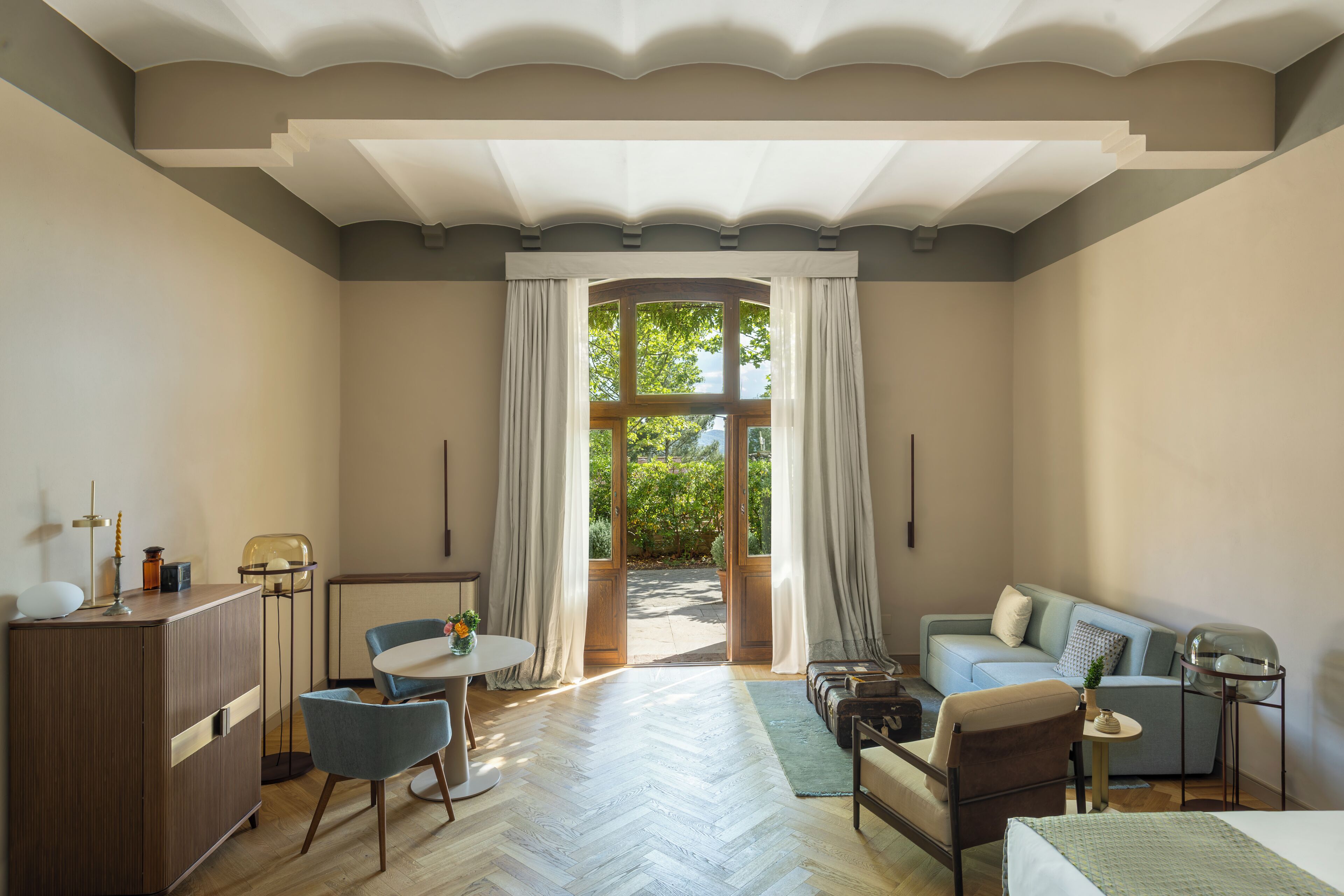 A room with a wooden floor, a sofa, a chair, a table, and a cabinet. There is a window with curtains.