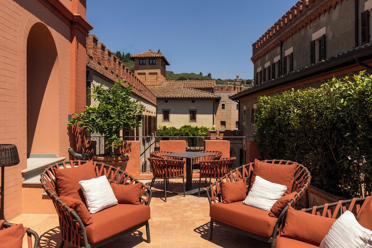 An outdoor patio with wicker furniture and a tiled floor, surrounded by buildings with red brick walls and tiled roofs.
