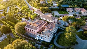 An aerial view of a historic building complex with multiple structures, including a central building with a courtyard, surrounded by lush greenery and a winding road. - Borgo Dei Conti Resort Relais & Chateaux (Perugia)