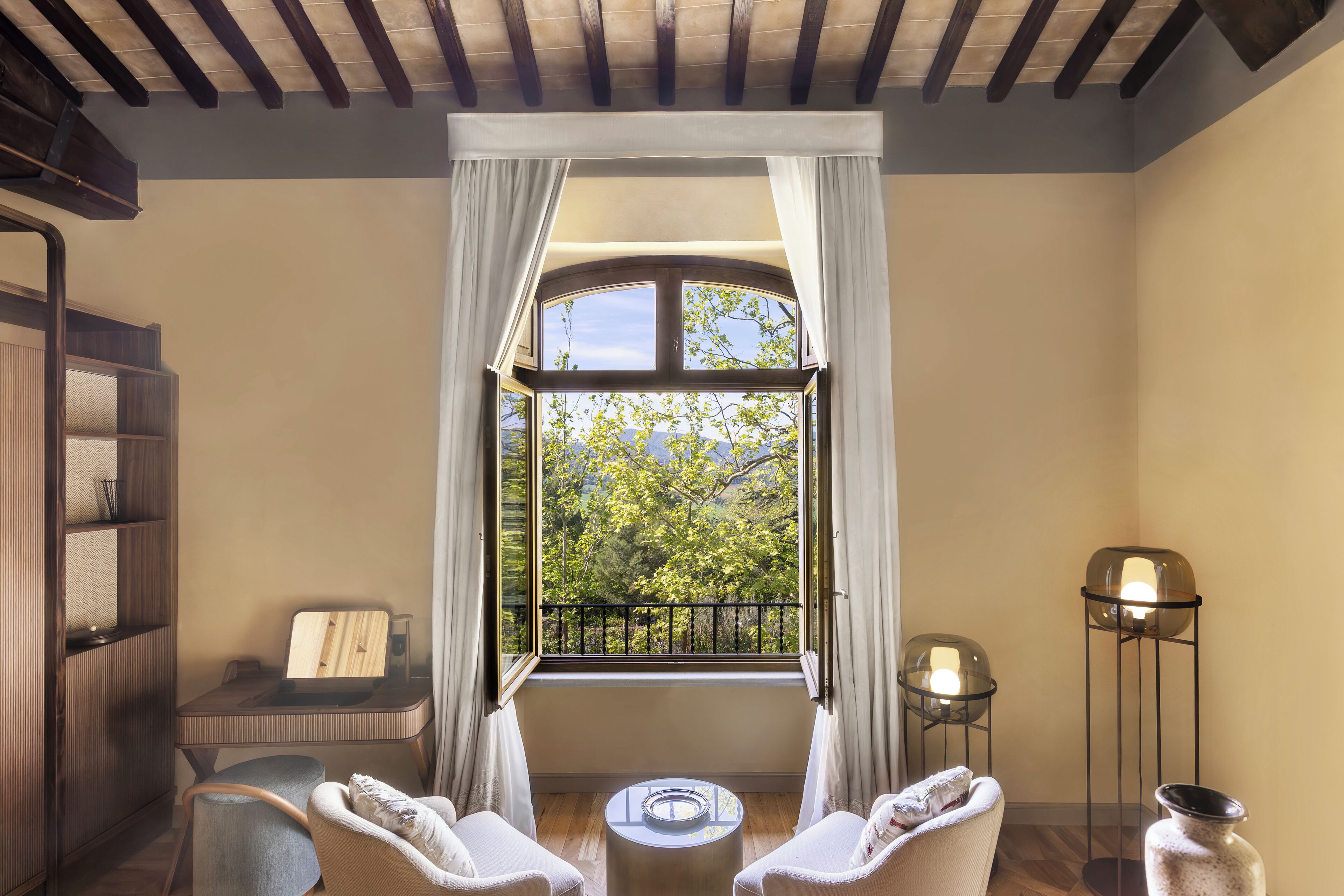Ein Zimmer mit großem Fenster, Schreibtisch, zwei Stühlen, einem kleinen Tisch und einer Stehlampe.
