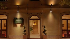 Entrada de hotel com balcão de recepção, escada e duas plantas em vasos.