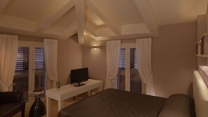 Quarto com uma cama, uma escrivaninha com computador, uma cadeira e uma janela com cortinas.