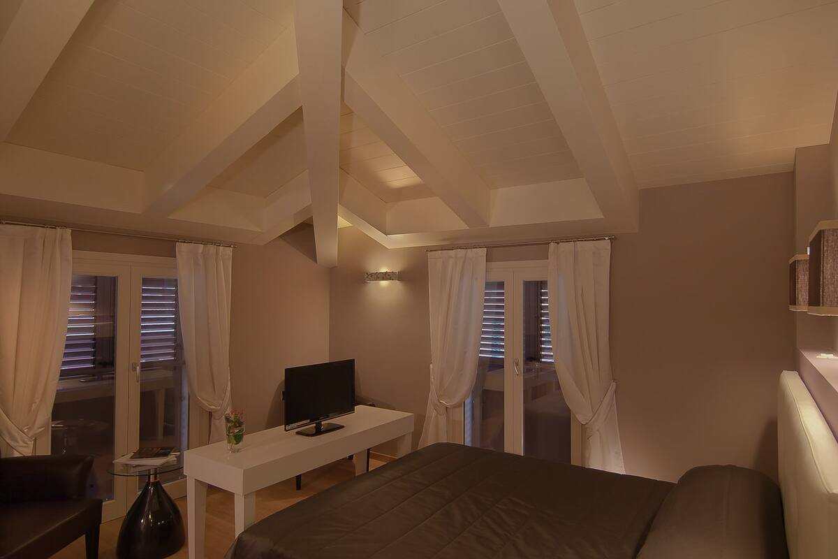A bedroom with a bed, a desk with a computer, a chair, and a window with curtains.