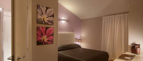 Ein Schlafzimmer mit Bett, Schreibtisch mit Stuhl, Nachttisch und einem Fenster mit Vorhängen.