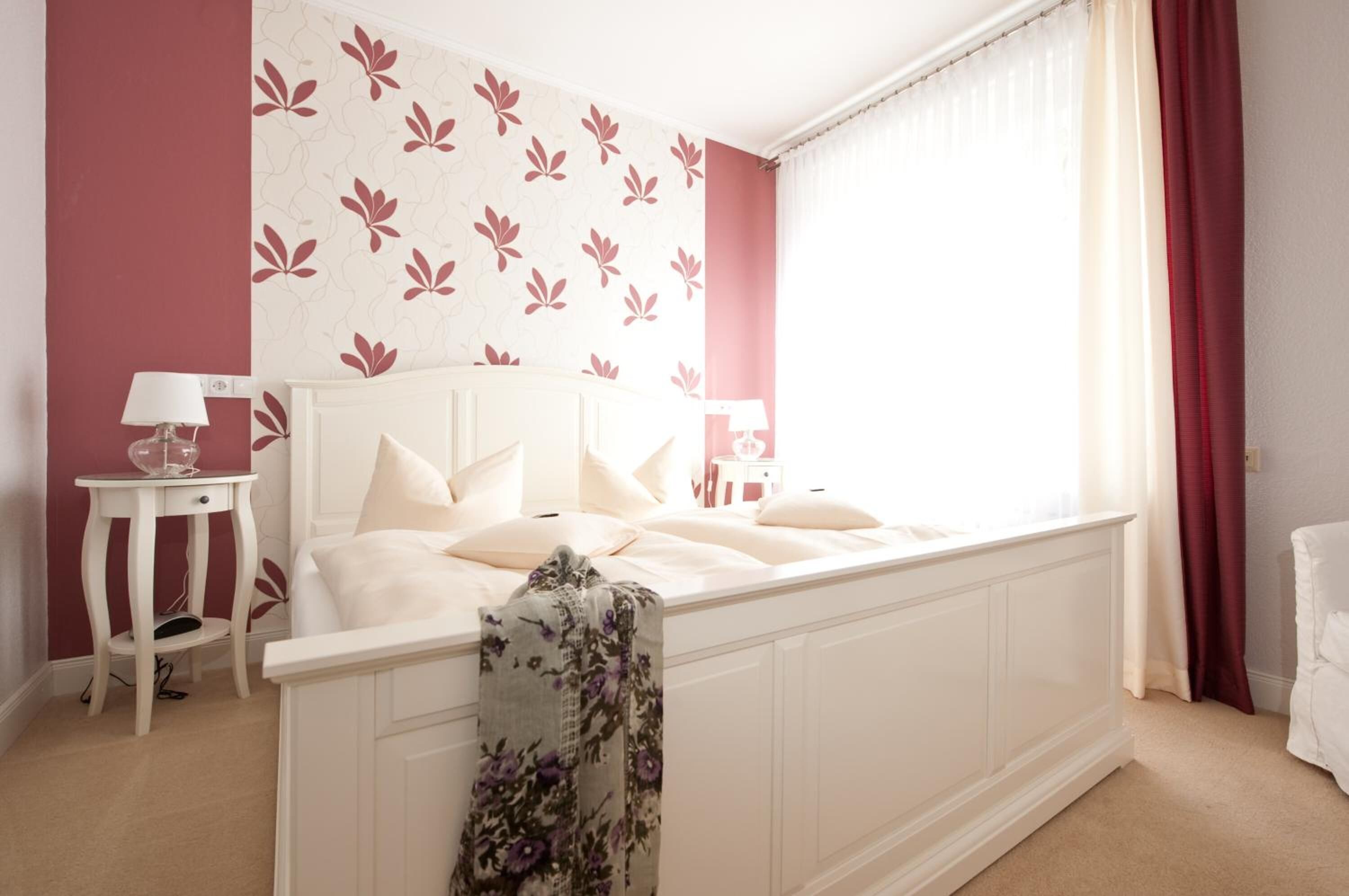 A bedroom with a bed, a nightstand, a lamp, and a window with curtains.
