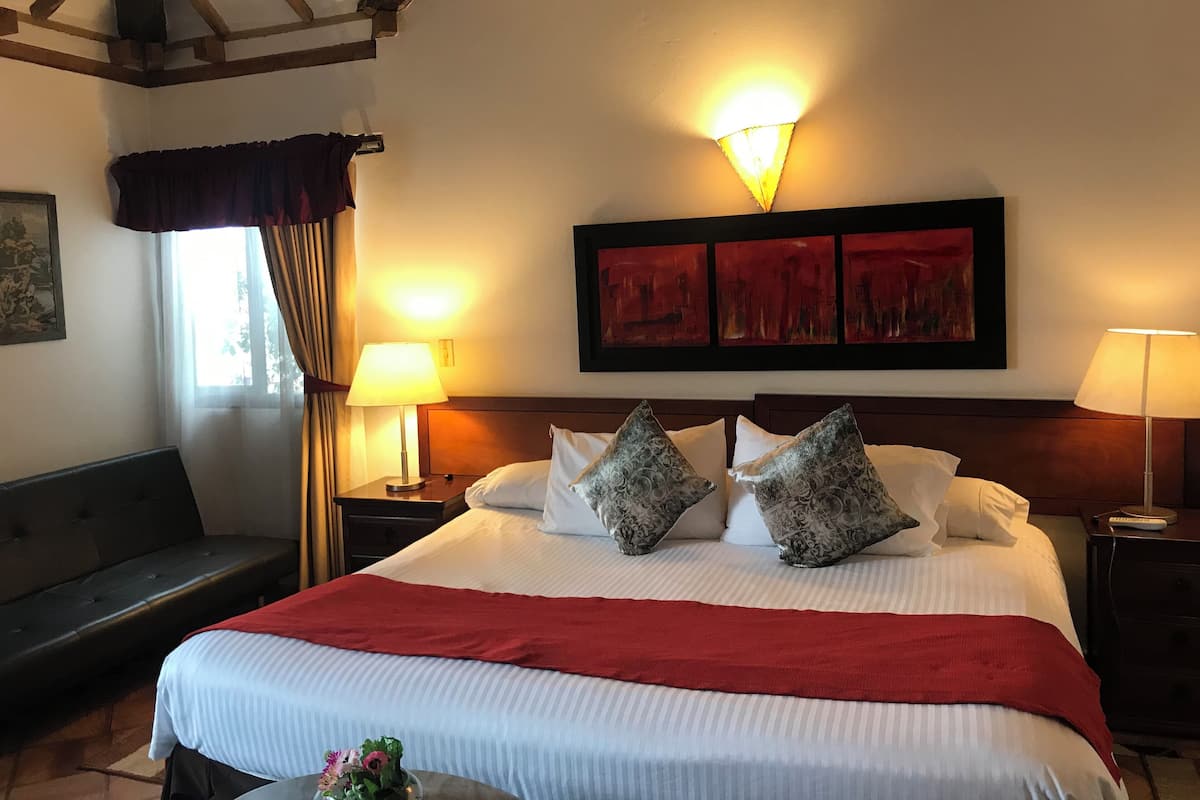 Una habitación de hotel con una cama grande, dos lámparas de noche, una colcha roja y un cuadro sobre la cama.