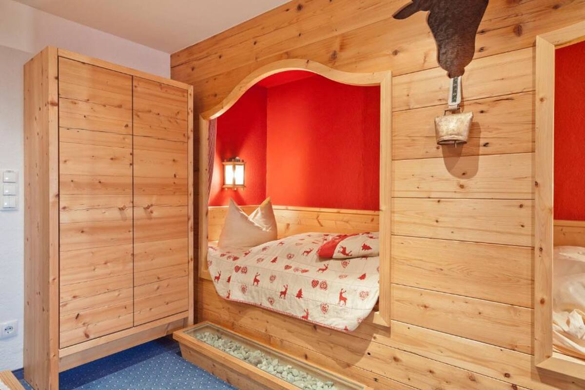Ein Zimmer mit Holzboden, einem Bett, einem Kleiderschrank und einem kleinen Fenster mit Nachttischlampe.