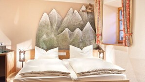 Cama de casal com roupa de cama branca, cabeceira de madeira e arte na parede com tema de montanhas.