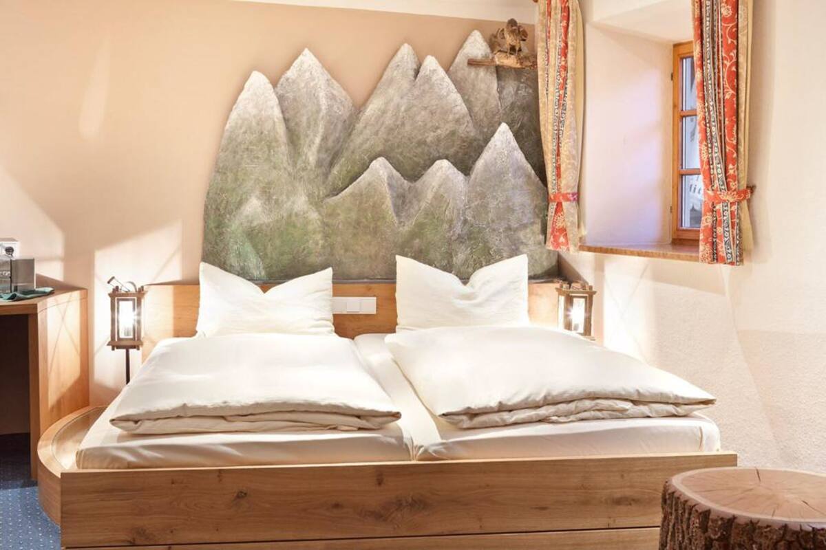 Ein Doppelbett mit weißer Bettwäsche, einem Holzkopfschild und Wandbildern mit Bergmotiven.