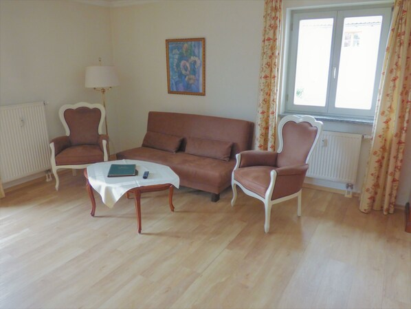 A living room with a brown sofa, two armchairs, a small table with a book and remote, a lamp, and a painting on the wall. - Gasthof Falkenstein & Metzgerei Schwaiger (Flintsbach A. Inn)