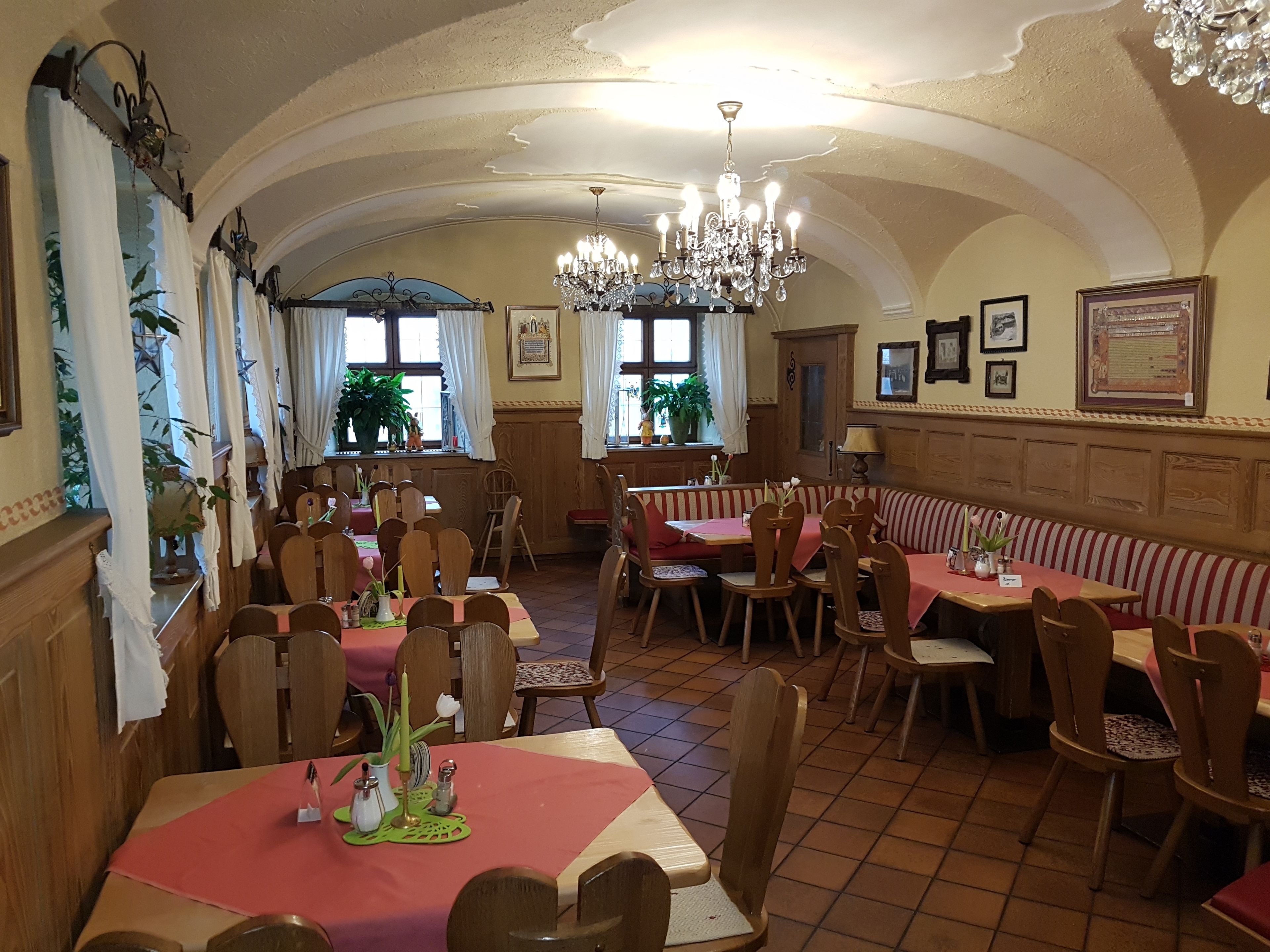 Ein Restaurant mit mehreren Tischen, Stühlen, einer Chandelüster und Topfpflanzen.