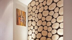 Um sofá marrom com almofadas vermelhas em um corredor com uma parede de lenha empilhada e um quadro na parede.