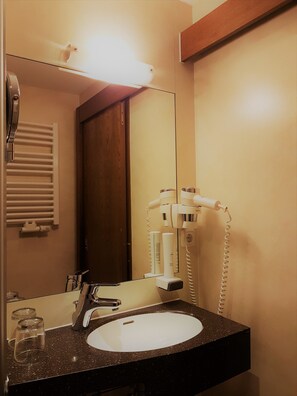 A bathroom with a sink, mirror, hairdryer, and towel rack.