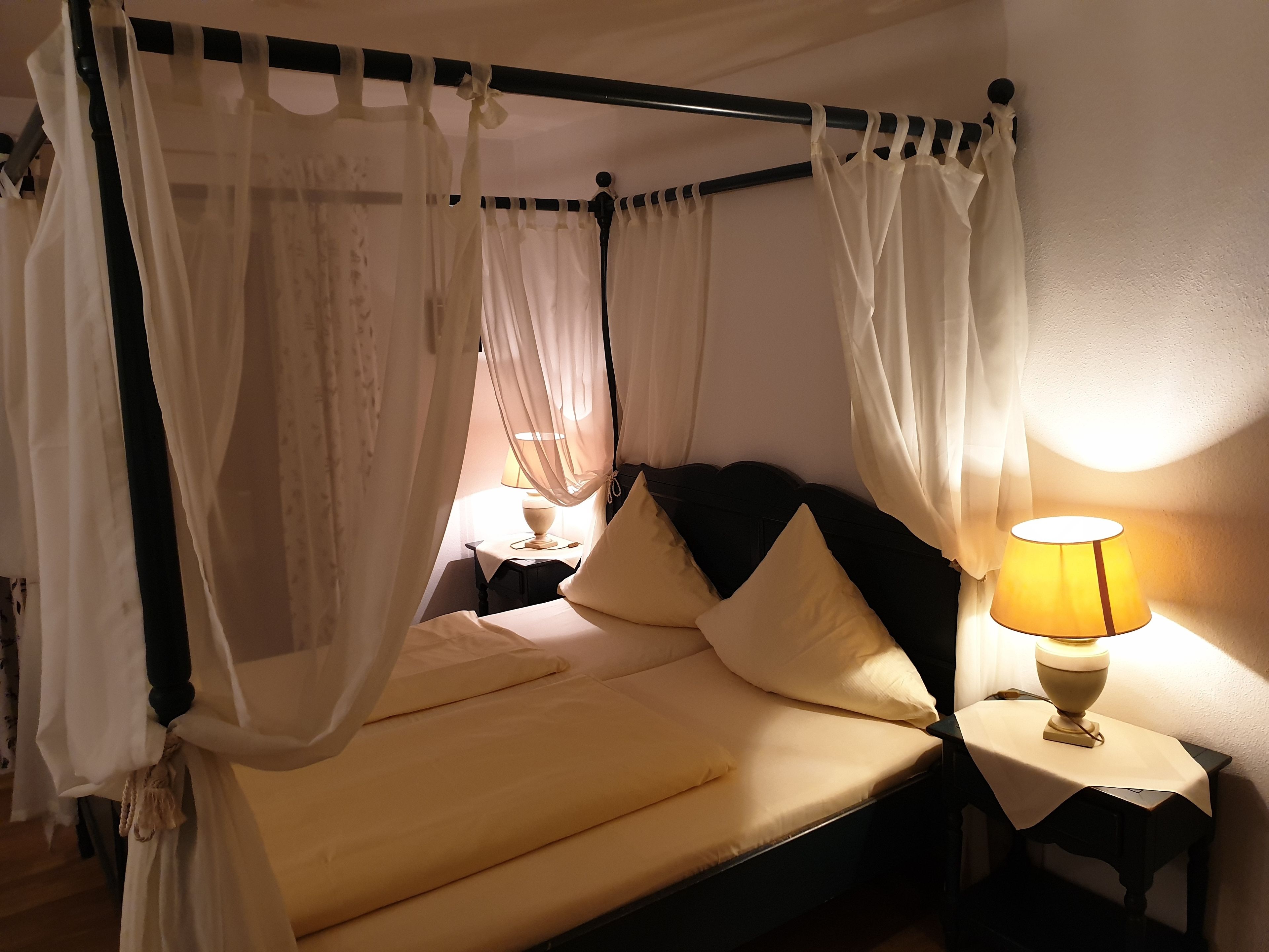 Een hemelbed, een nachtkastje met lamp en een tweede nachtkastje.