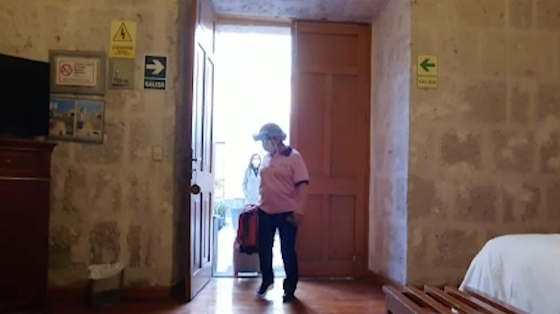 Un pasillo con una puerta de madera, un letrero que indica una dirección y una persona de pie cerca de la puerta.