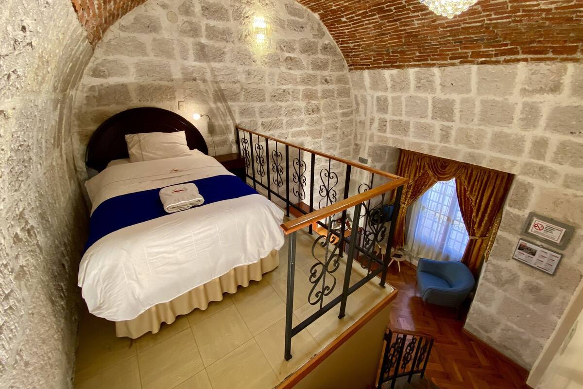 Una habitación acogedora con pared de piedra, cama de madera, baranda de metal y una silla azul.
