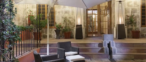 An outdoor patio with wicker furniture, a large umbrella, and potted plants.