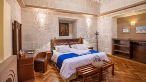 A bedroom with a large bed, wooden furniture, a chandelier, and a stone wall. - Hotel Casona Solar (Arequipa)