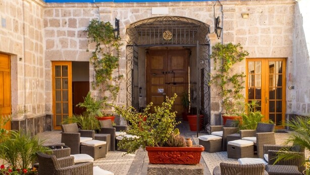 A courtyard with stone walls, a wooden door, wicker furniture, and potted plants. - Hotel Casona Solar (Arequipa)