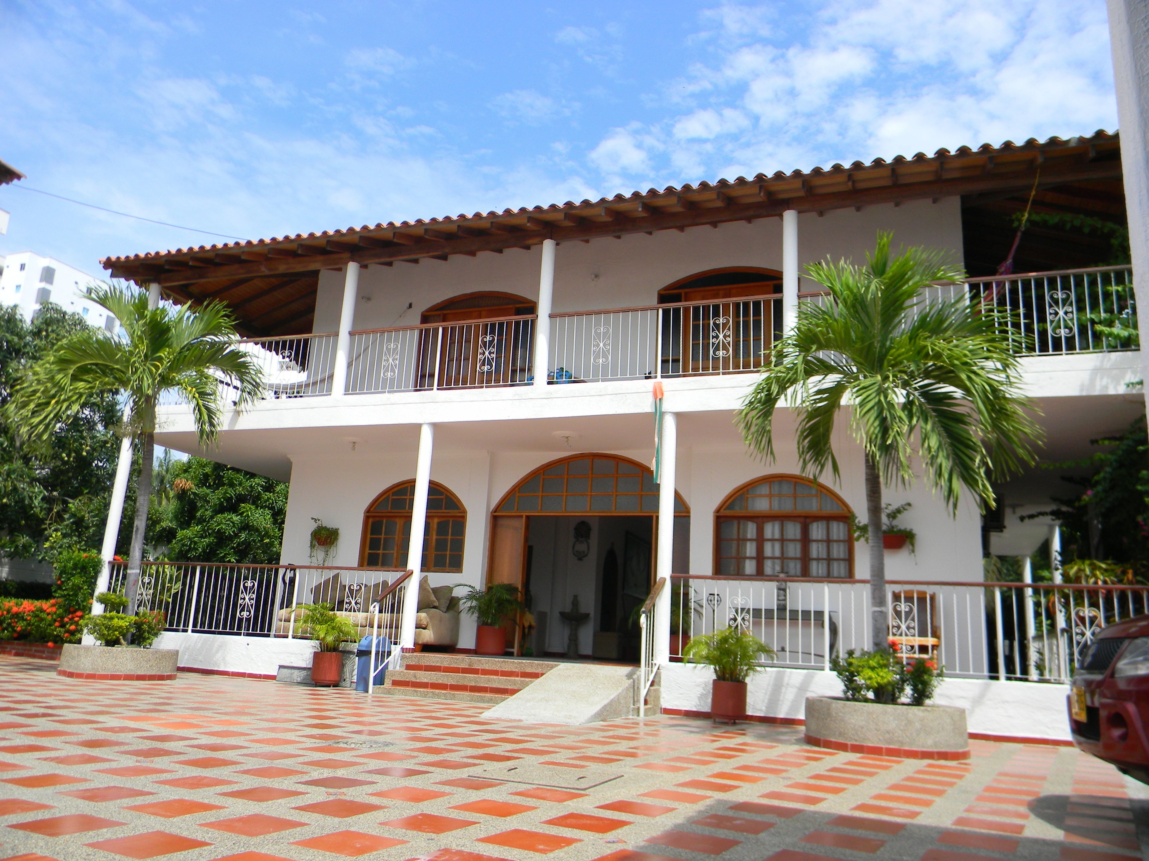 A two-story building with a balcony, potted plants, and a tiled entrance area.
