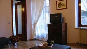 A living room with a sofa, a small table with a tray, a television on a cabinet, a door, and a window with curtains. - B&B La Nara (Turin)