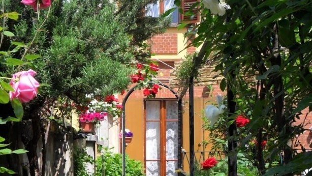 A narrow pathway flanked by lush greenery and flowering plants leading to a building with a tiled entrance. - B&B La Nara (Turin)
