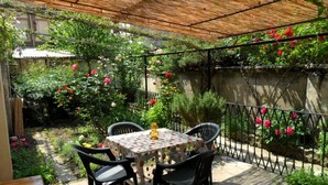 A patio with a table and chairs, surrounded by a garden with flowering plants and a metal fence. - B&B La Nara (Turin)