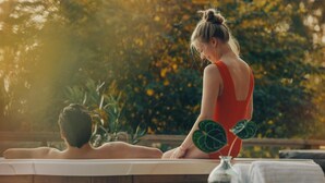 Eine Person im roten Badeanzug sitzt an einem Pool mit einem Kind.