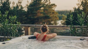 Eine Person entspannt sich in einer Hot Tub mit Blick auf Bäume und eine Holzterrasse.