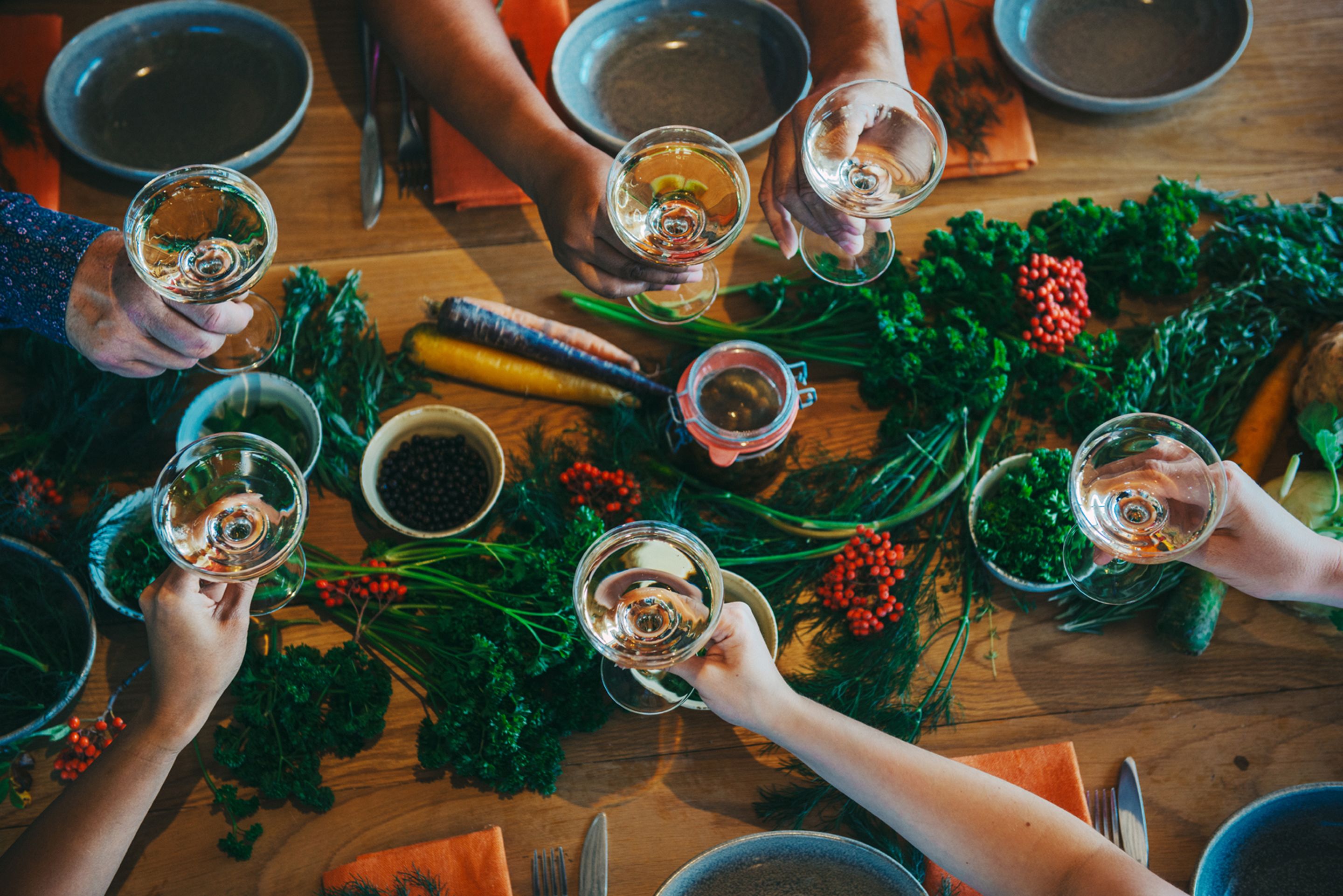 Un groupe de personnes est assis autour d’une table, devant des verres à vin, et est entouré de différents légumes et herbes aromatiques.