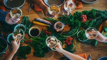 Un groupe de personnes est assis autour d’une table, devant des verres à vin, et est entouré de différents légumes et herbes aromatiques.