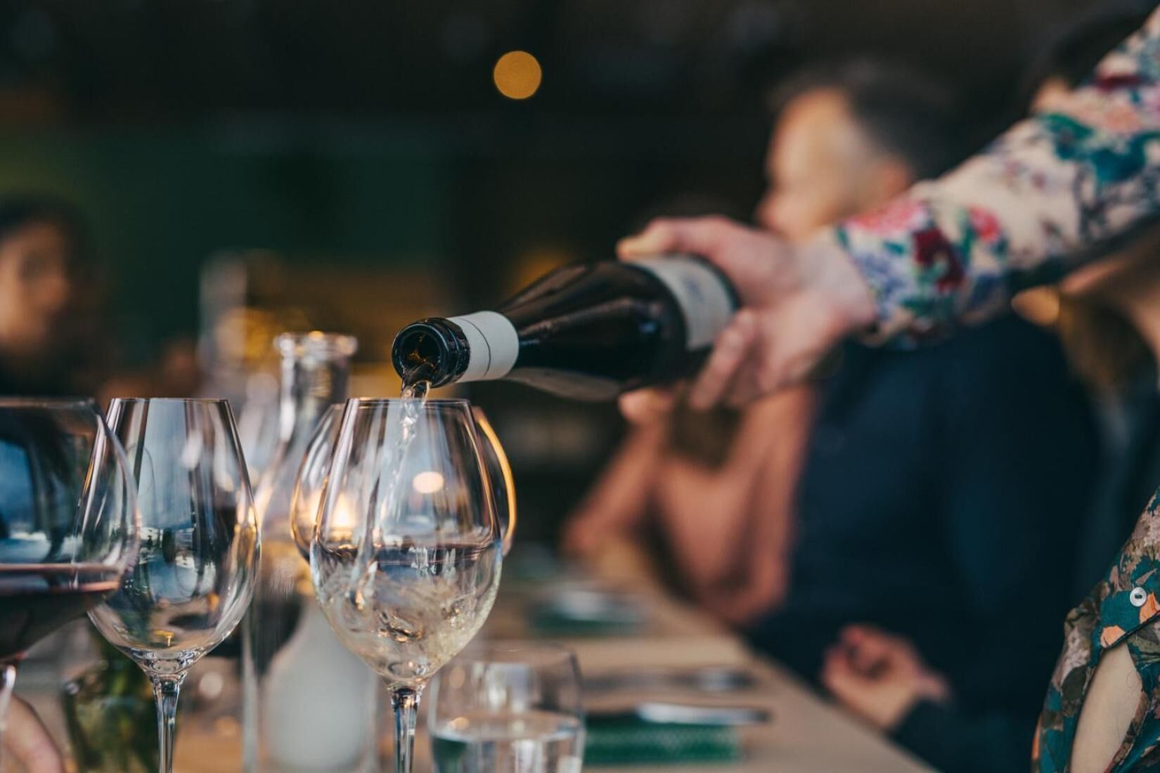 Une personne verse du vin dans un verre à une table à manger.