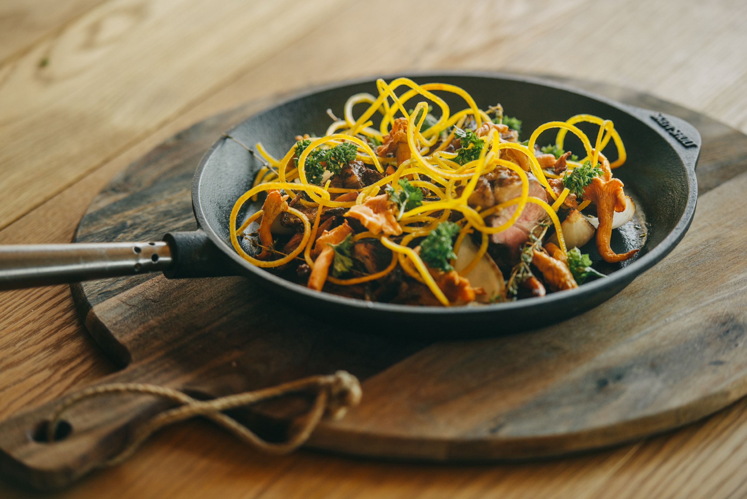 A skillet with a stir-fry dish on a wooden board.
