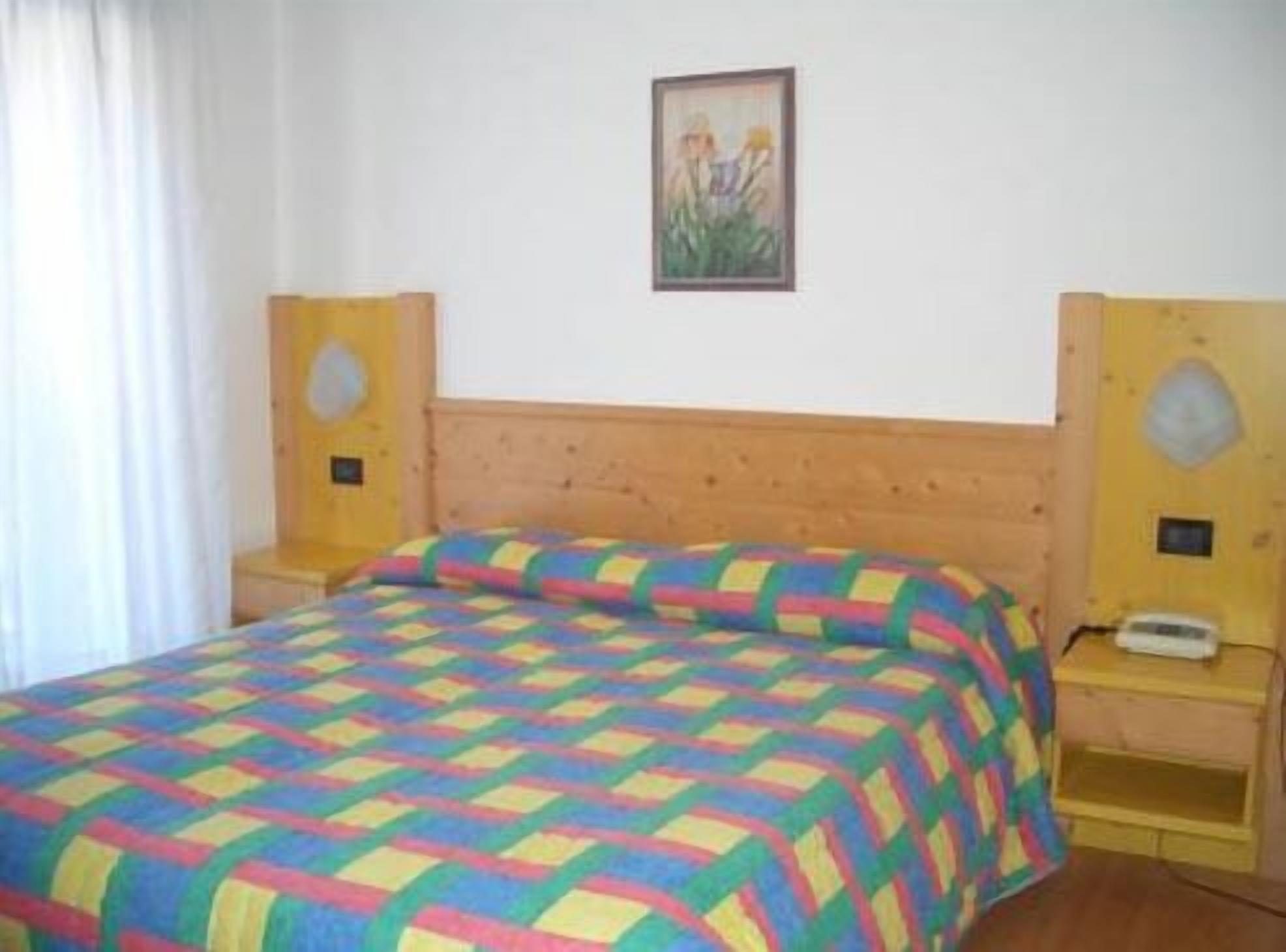 A bedroom with a wooden bed, colorful quilt, two bedside tables, a nightstand, and a painting on the wall.