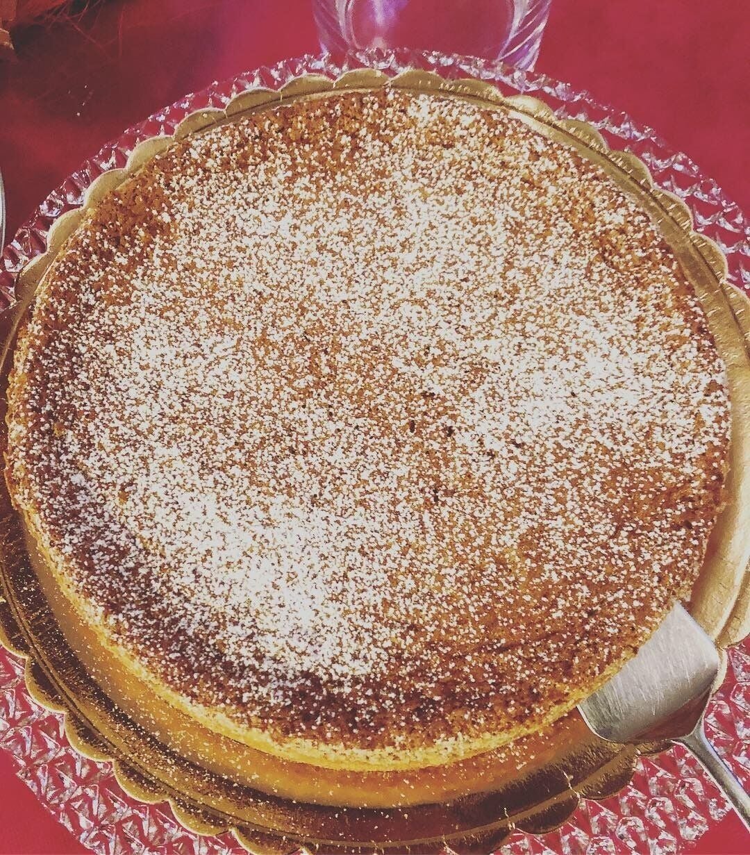 A pie on a glass plate with a golden rim, placed on a red tablecloth.