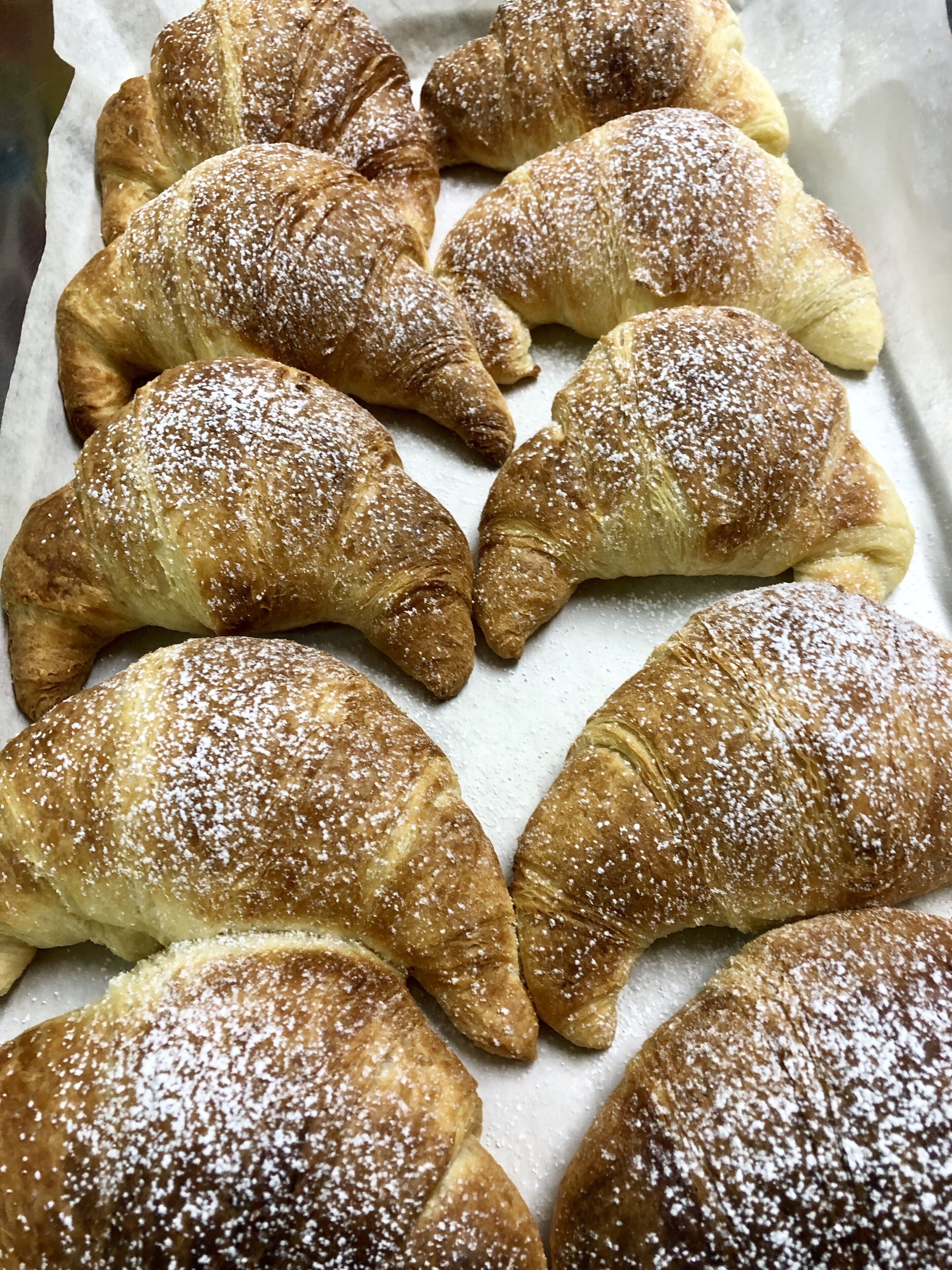 Eine Schale mit frisch gebackenen Croissants, bestäubt mit Puderzucker.