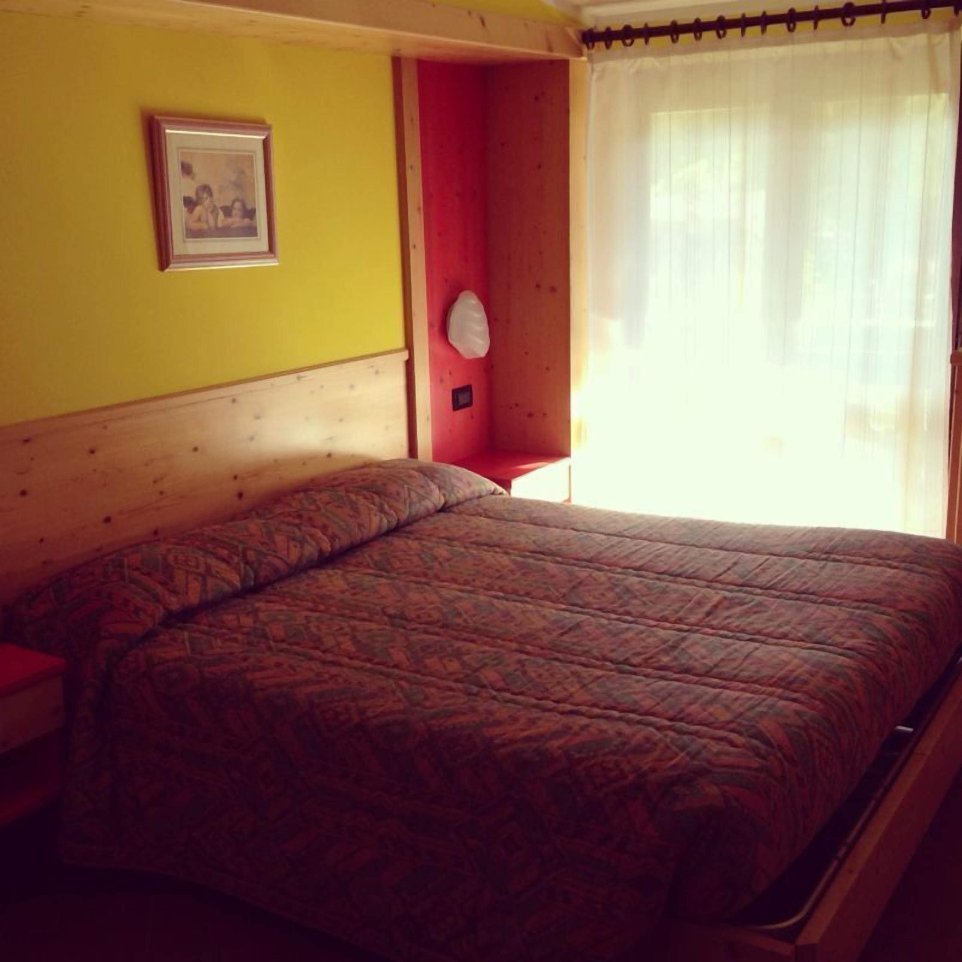 A bed in a room with a wooden headboard, a red wall, and a white curtain.