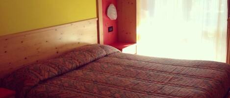 A bed in a room with a wooden headboard, a red wall, and a white curtain.