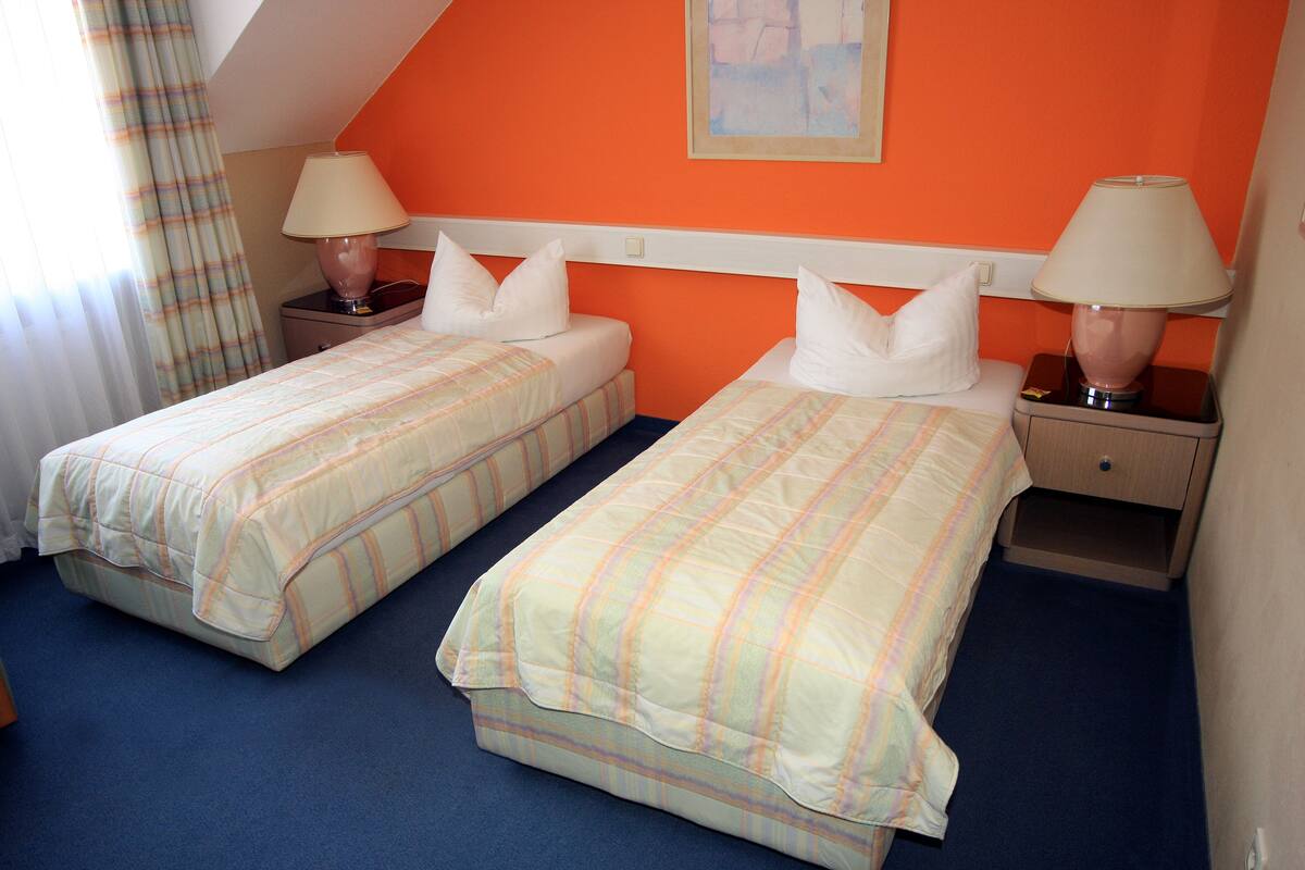 A hotel room with two beds, each with a matching nightstand and lamp.