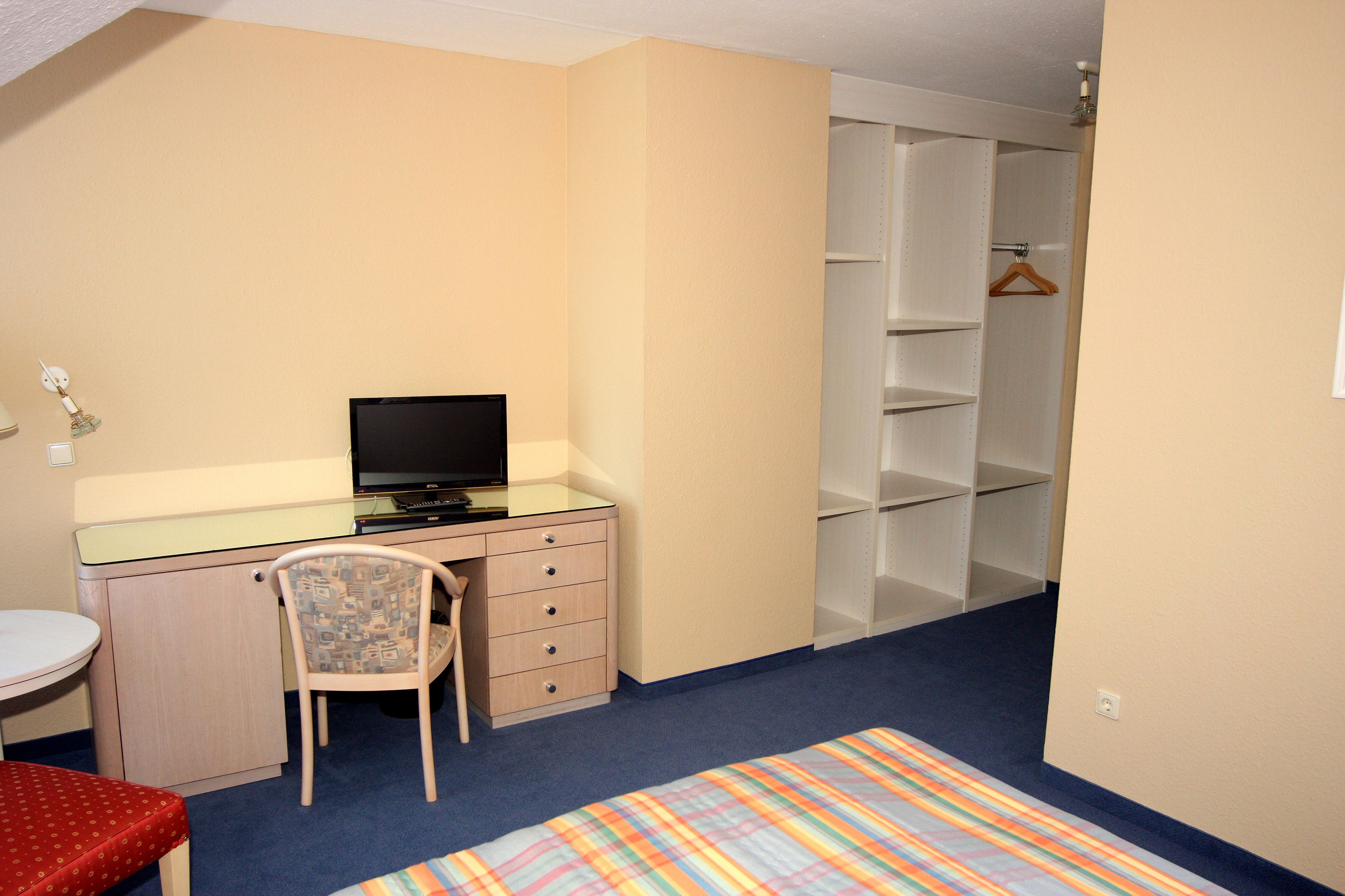 A bedroom with a bed, a desk with a chair, a television, and a closet.