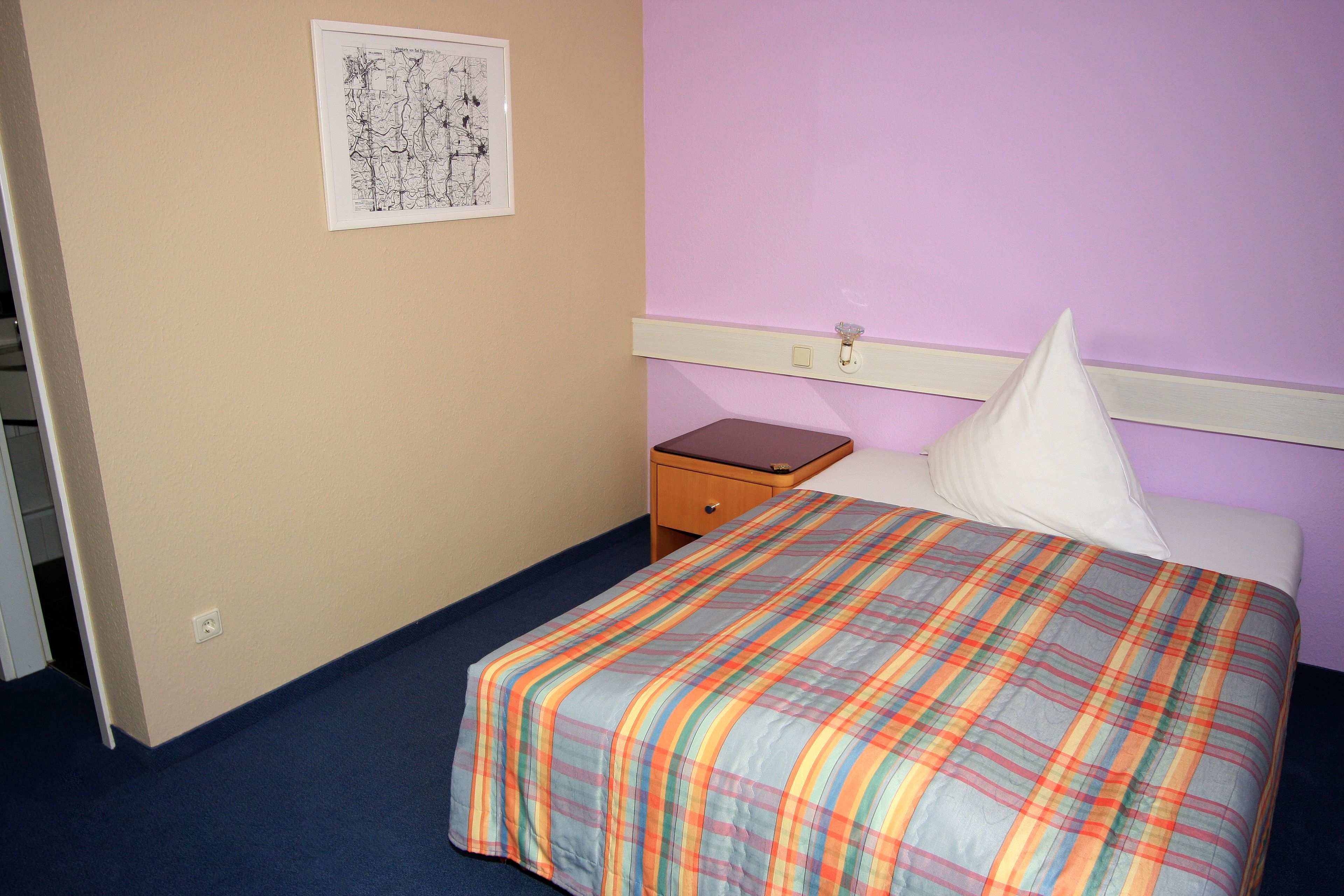 A hotel room with a bed, a nightstand, a dresser, and a wall-mounted light switch.