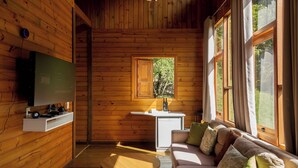 L’intérieur d’un chalet accueillant, avec un revêtement mural en bois, un canapé avec des coussins, une petite table, un téléviseur fixé au mur et une fenêtre avec des rideaux.