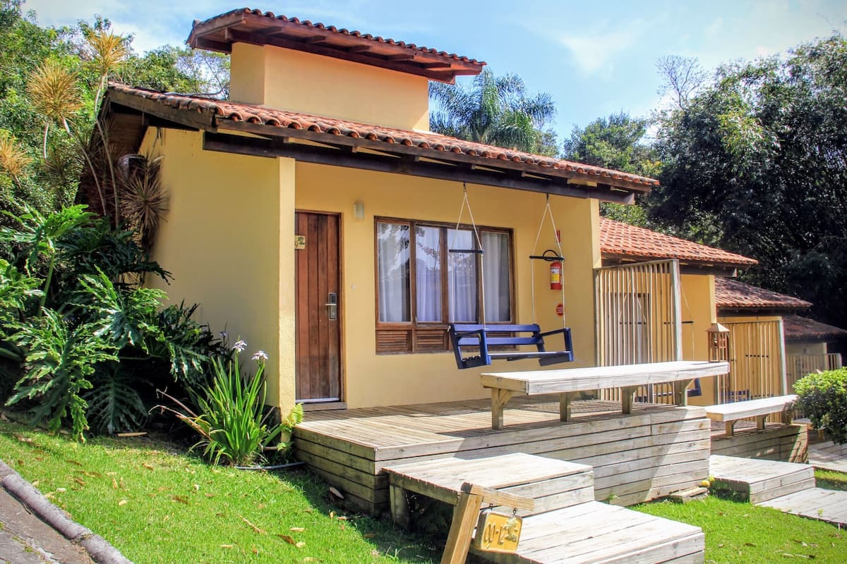 A yellow building with a red-tiled roof, a wooden deck, and a bench.